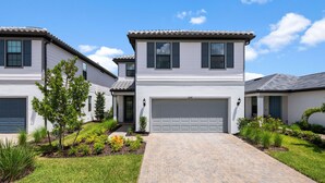 A two-story house with a garage, a paved driveway, and a well-maintained lawn with various plants.