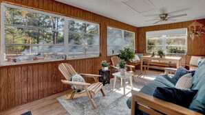 L’intérieur chaleureux d’un chalet avec des murs en bois, de grandes fenêtres, un ventilateur de plafond et un banc en bois.