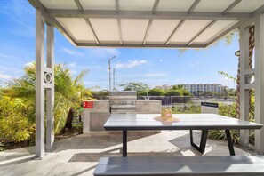 Eine Terrasse im Freien mit einem Grill, einem Tisch mit einem Hut und Blick auf Gebäude im Hintergrund.