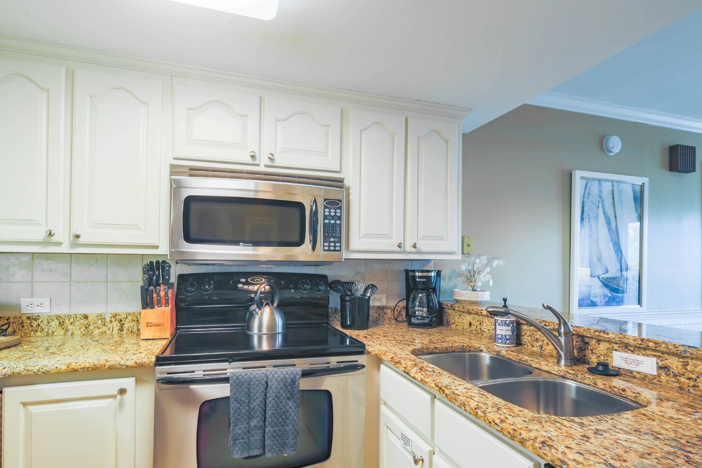 A kitchen with white cabinets, stainless steel appliances, granite countertops, and a double sink.