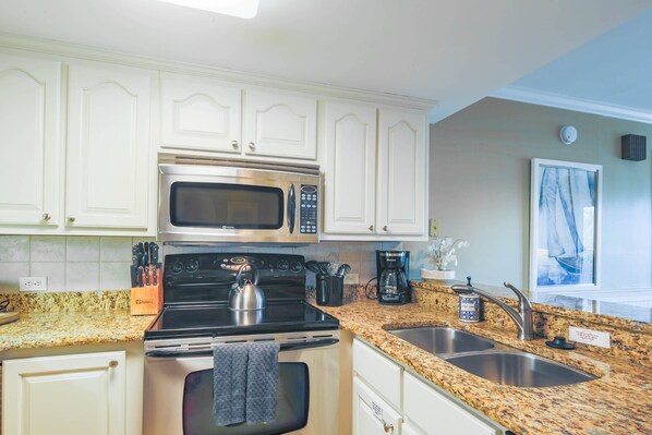 A kitchen with white cabinets, stainless steel appliances, granite countertops, and a double sink.