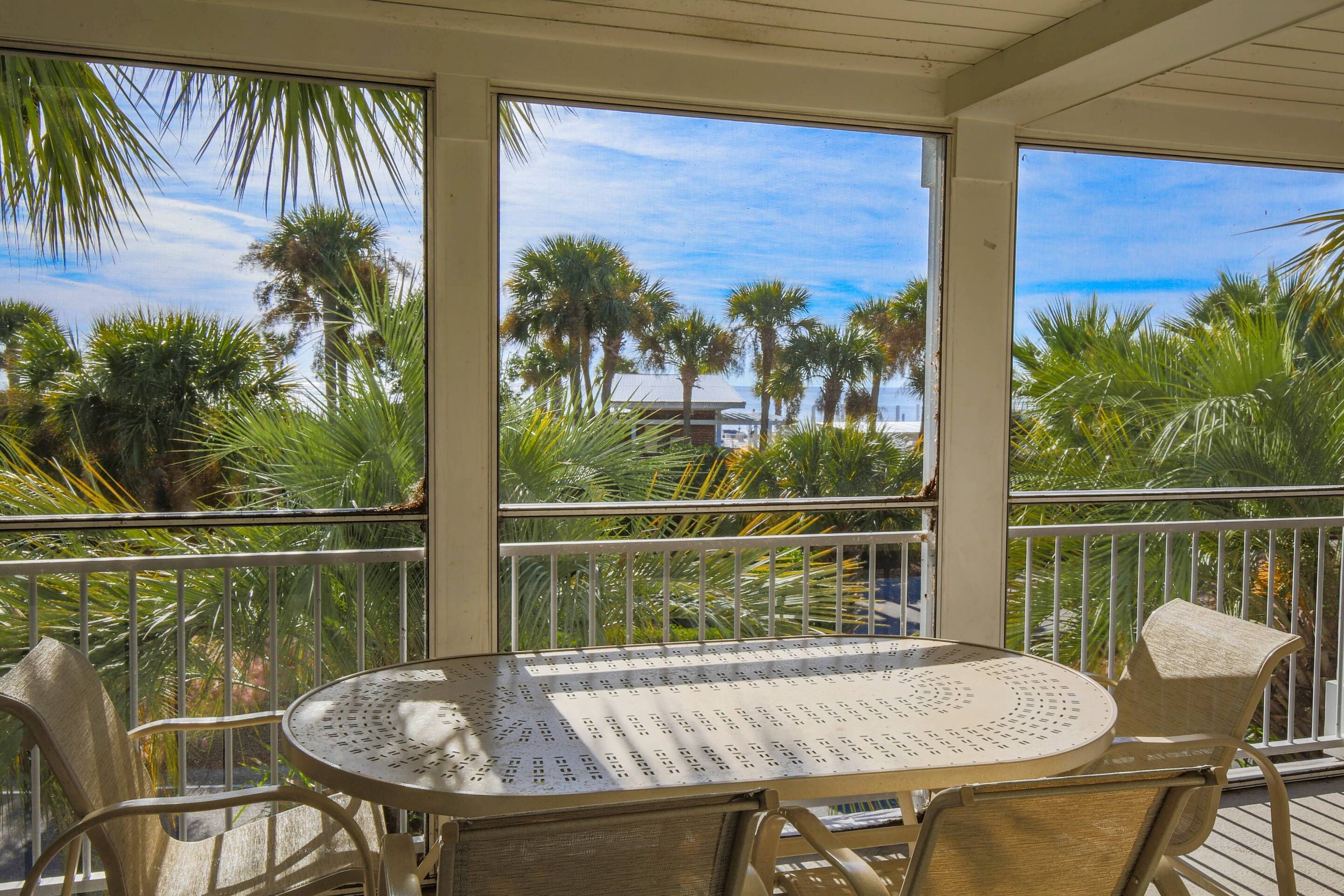 Un balcon avec une table ronde et des chaises, d’où l’on peut admirer des palmiers et un ciel dégagé.