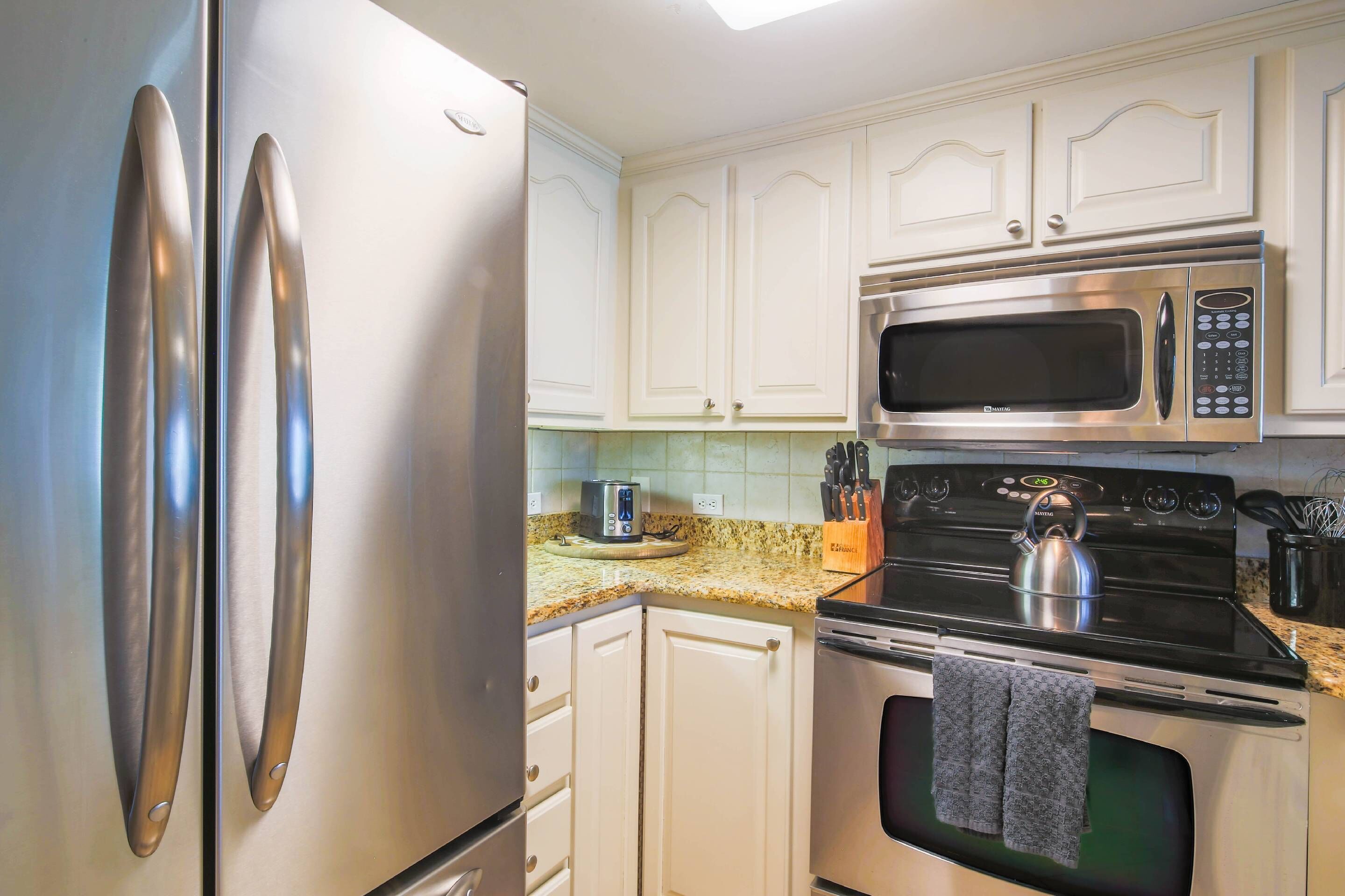 A kitchen with white cabinets, stainless steel appliances, a microwave, a kettle, and a toaster.