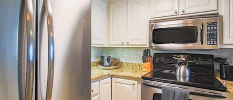 A kitchen with white cabinets, stainless steel appliances, a microwave, a kettle, and a toaster.