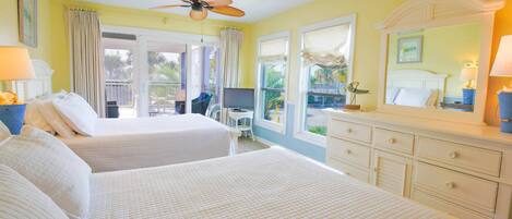 A hotel room with two beds, a ceiling fan, a TV, and a balcony with a view of the outdoors.
