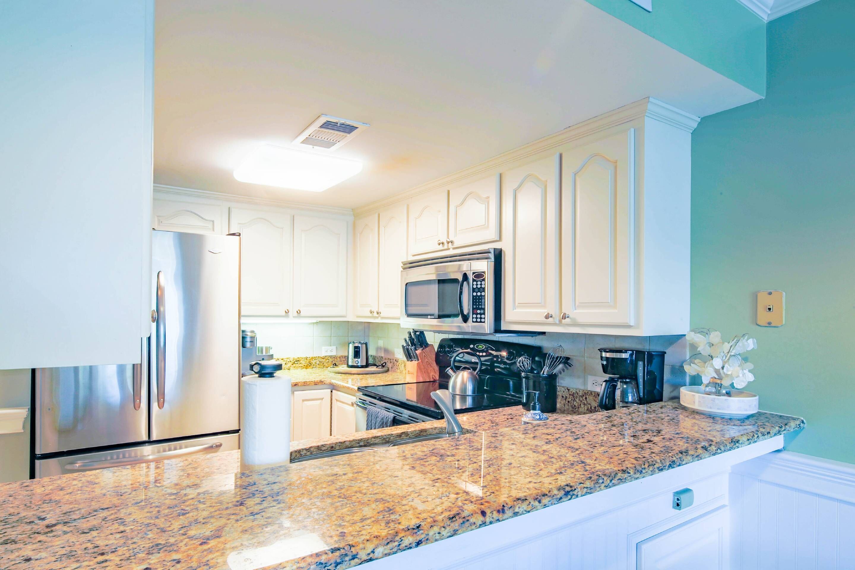 A kitchen with white cabinets, a stainless steel refrigerator, a microwave, and a granite countertop.