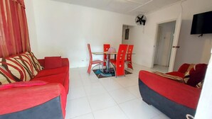 Un salon avec deux canapés rouges, une table basse en verre et un coin repas avec des chaises rouges.
