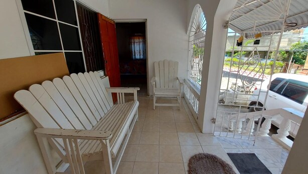 Une véranda avec un banc blanc, une chaise et une table entourée de chaises.