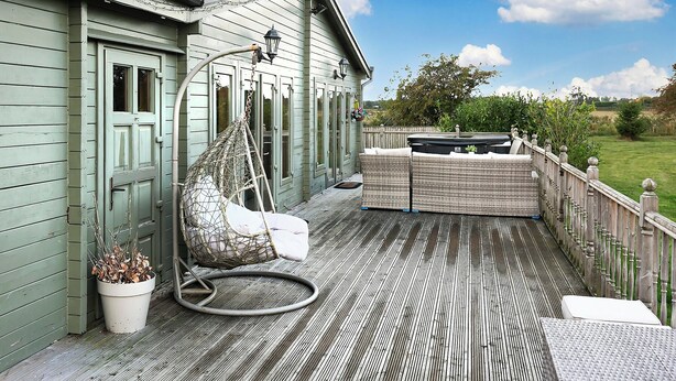A wooden deck with a hanging chair, a cushioned bench, and a potted plant. - Sleeps6- Hot Tub- Pet Friendly- Log Burner (York)