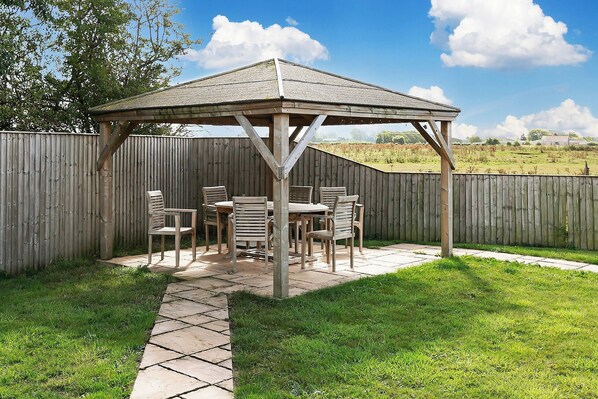 Un gazebo de madera con una mesa y sillas en un patio trasero.