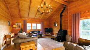 A cozy cabin interior with a wooden ceiling, a fireplace, a sofa, a TV, and a dining area. - Sleeps6- Hot Tub- Pet Friendly- Log Burner (York)