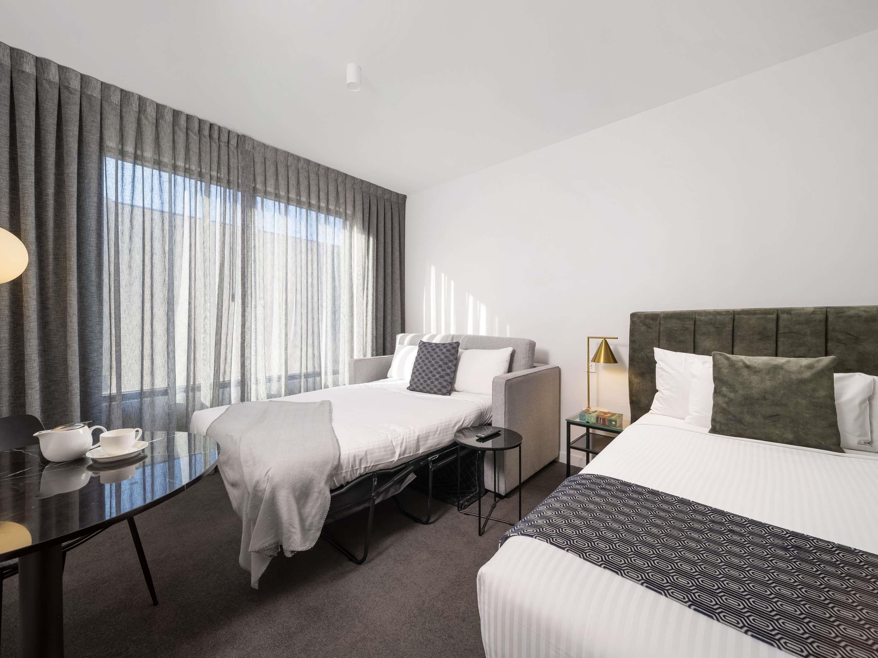 Ein Hotelzimmer mit zwei Betten, einem Schreibtisch, einem Stuhl, einer Lampe und einem fenster mit Vorhängen.