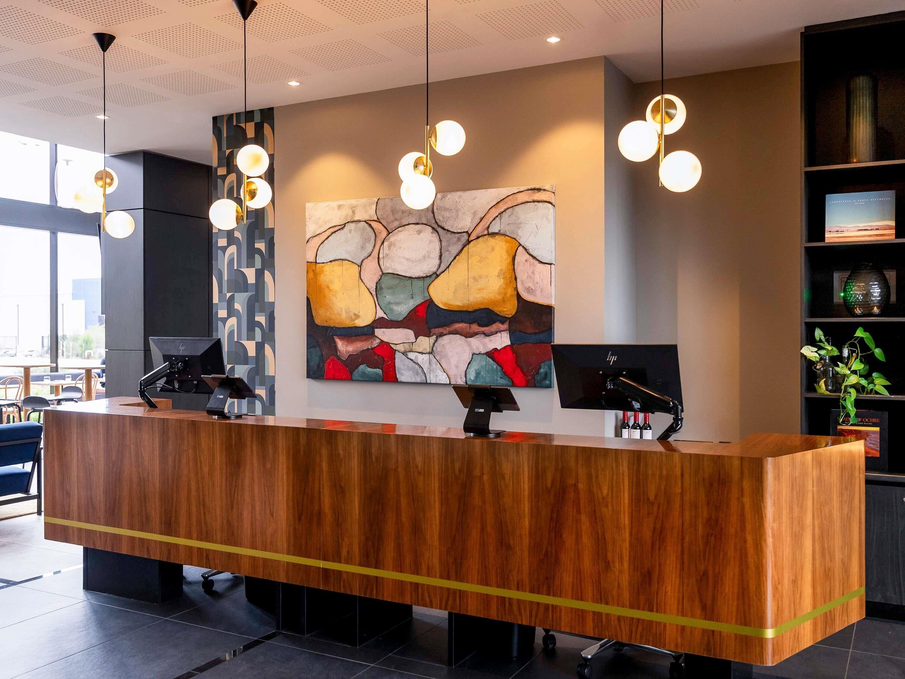 A reception desk with a wooden finish, two computer monitors, and a colorful abstract painting on the wall.