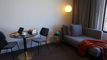 A hotel room with a round table, two chairs, a sofa, a lamp, and a window with curtains.