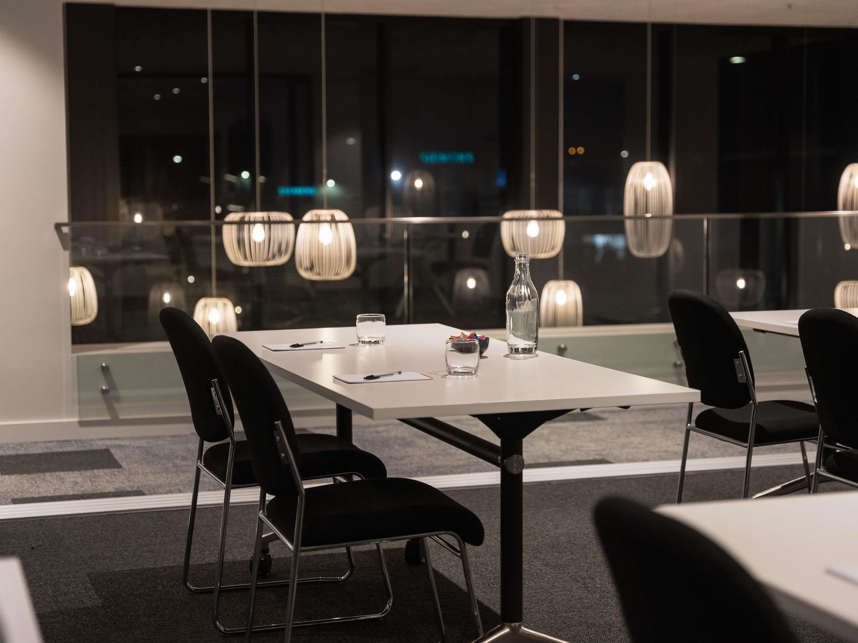 A modern conference room with glass walls, black chairs, a white table, and pendant lighting.