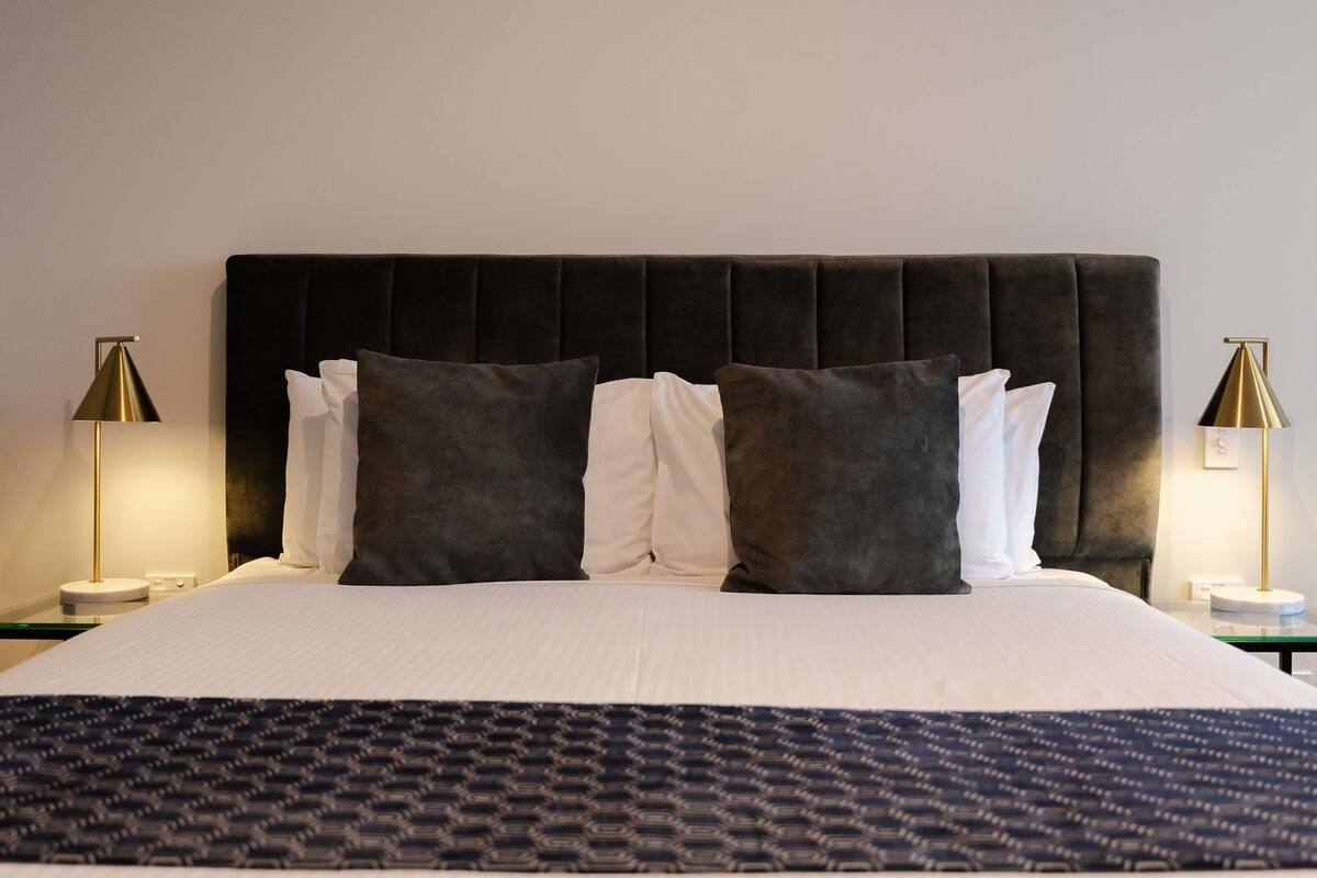 A hotel room with a large bed, two bedside lamps, and a dark headboard.