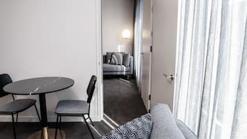 A modern hotel room with a round table, two chairs, a sofa, and a view of a balcony.