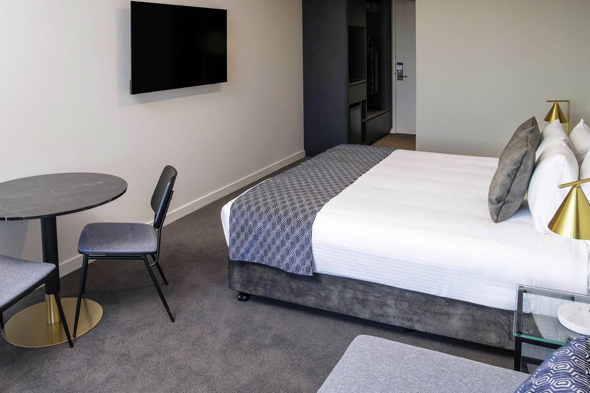 A hotel room with a bed, a TV, a small table, and a chair.