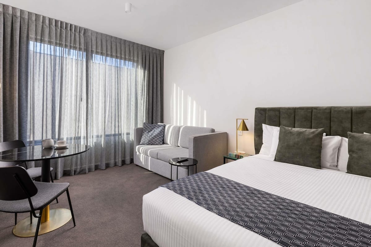 A hotel room with a bed, a sofa, a dining table with chairs, and a lamp.