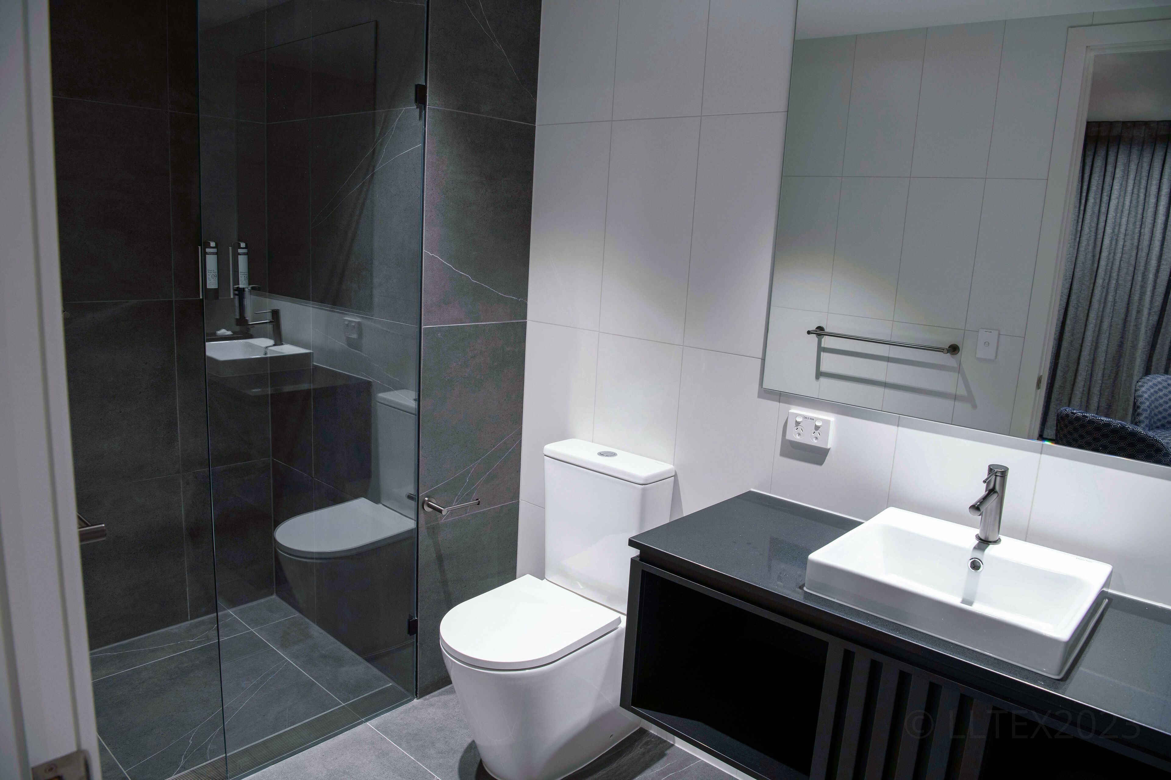 Een moderne badkamer met een douchecabine van glas, een wit toilet en een zwart badkamermeubel met een wastafel.