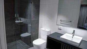 Een moderne badkamer met een douchecabine van glas, een wit toilet en een zwart badkamermeubel met een wastafel.
