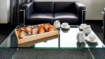 Uma mesa com tampo de vidro, com doces e jogos de chá, em um quarto moderno com sofá de couro preto.