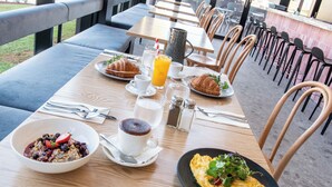 A breakfast setting with croissants, a bowl of cereal, a coffee, a glass of orange juice, and an omelette on a wooden table. - Mantra Tonsley Adelaide (Tonsley)