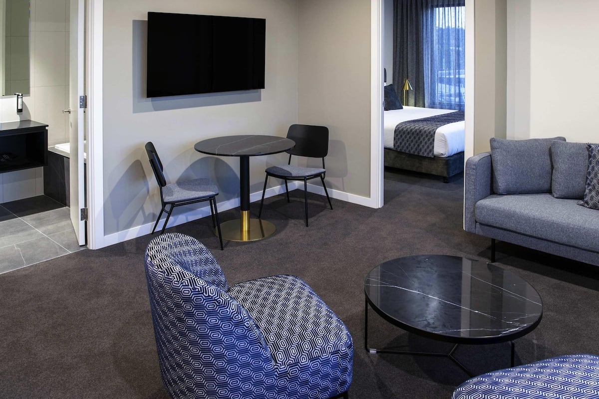 A modern hotel room with a sofa, two chairs, a small table, a TV, and a bed.
