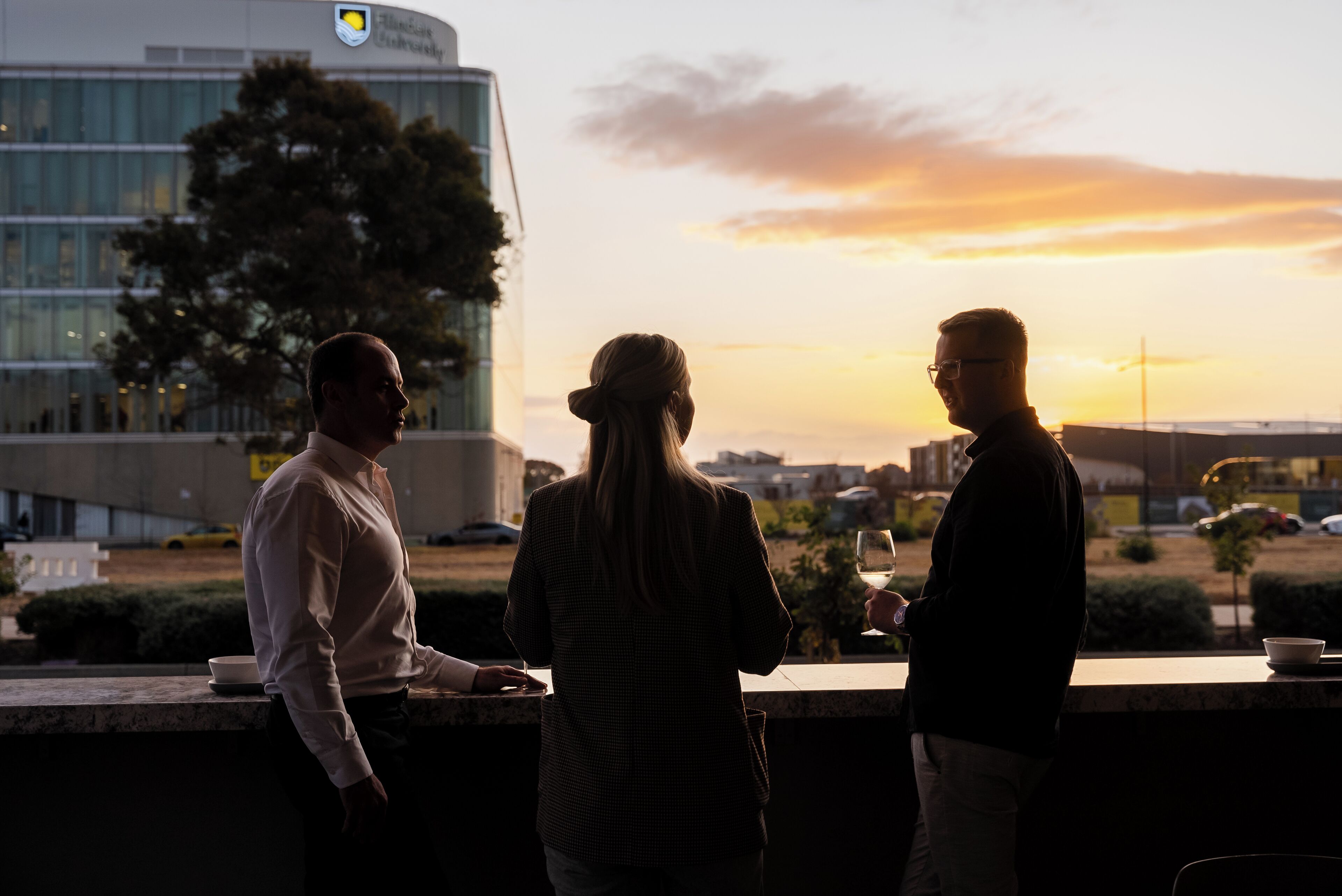 Three people standing at a bar with a sunset view.