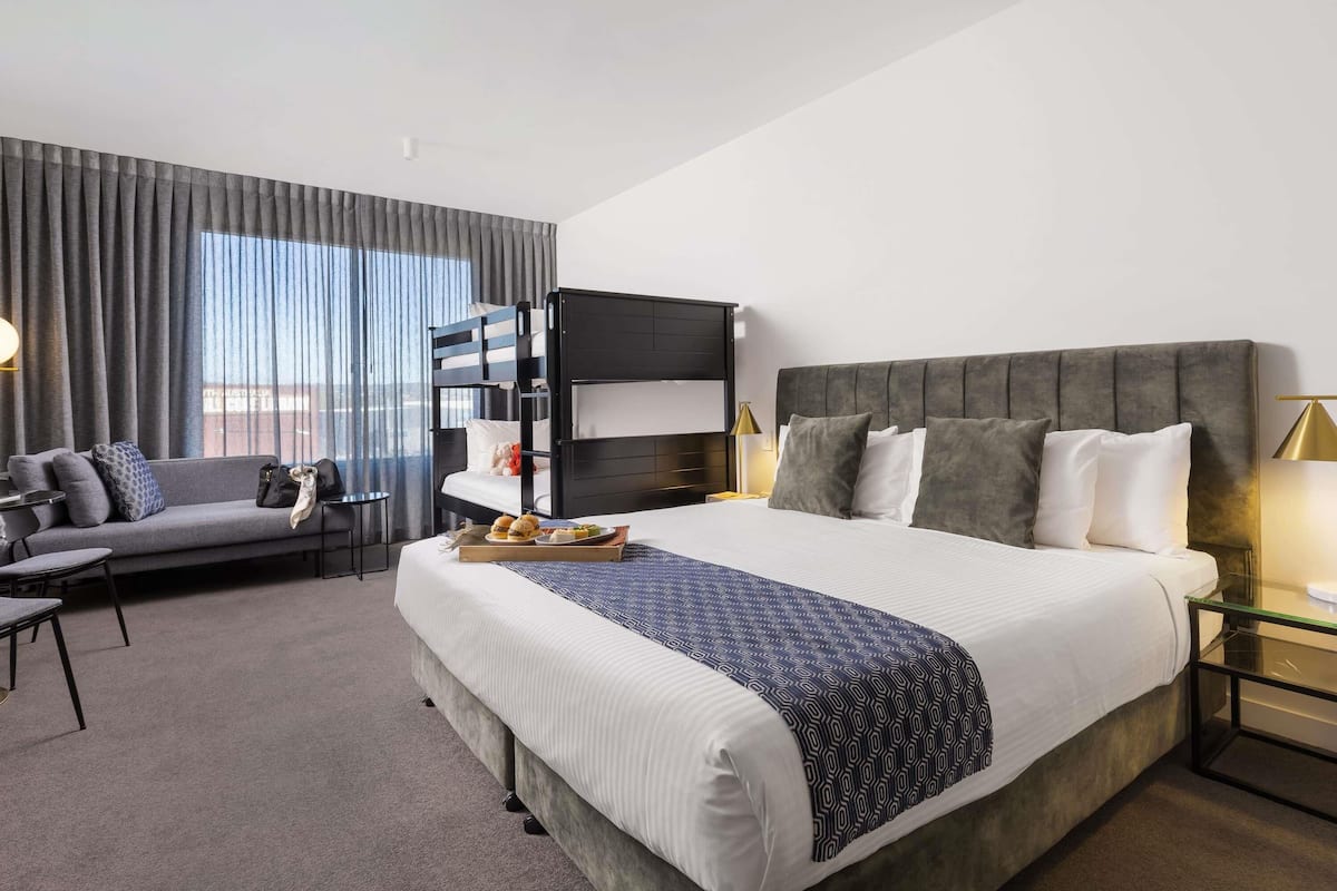 A hotel room with a bunk bed, a sofa, a desk, and a view of the city.