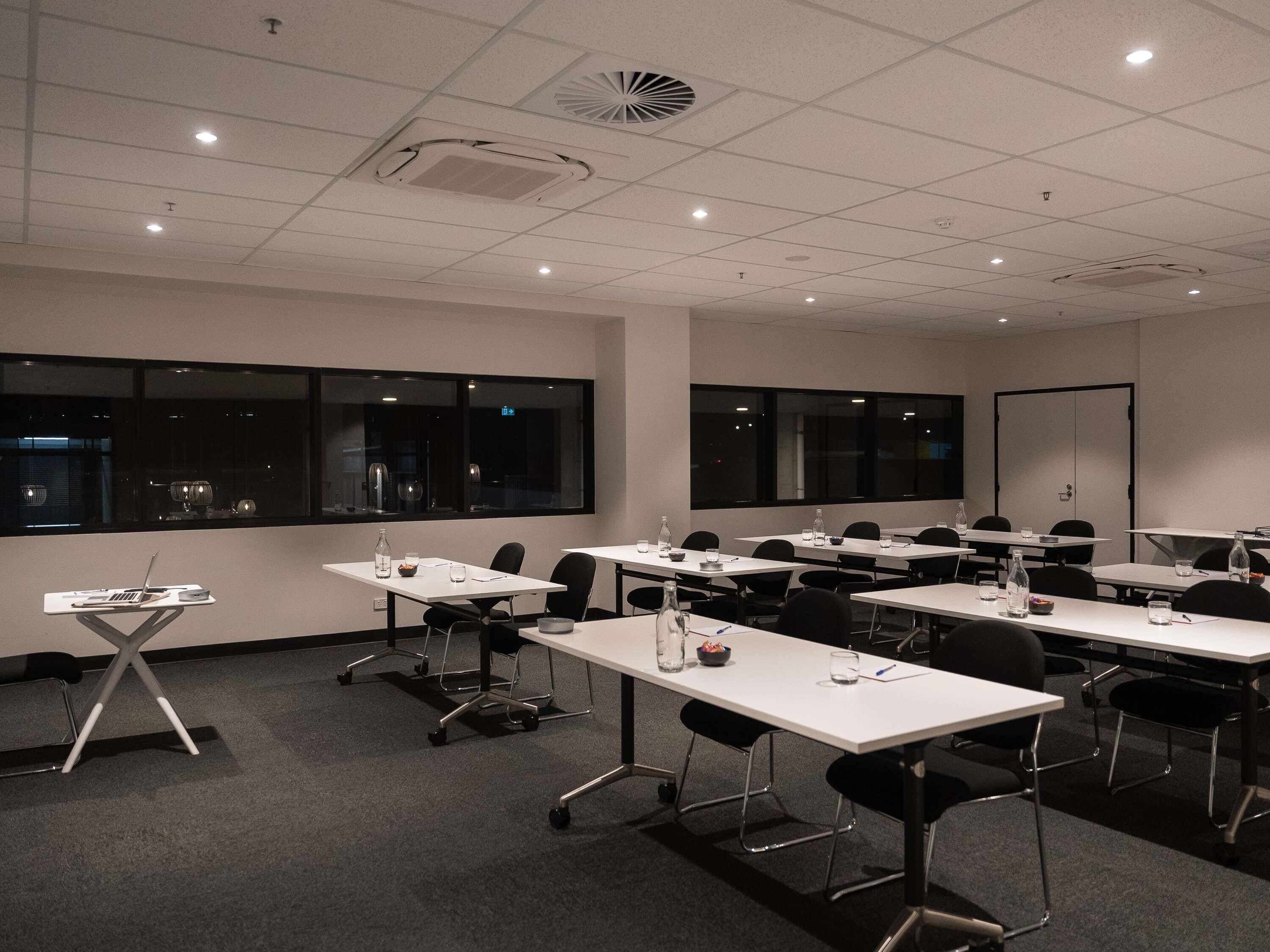 A conference room with tables, chairs, and a projector screen.