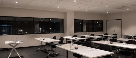 A conference room with tables, chairs, and a projector screen.