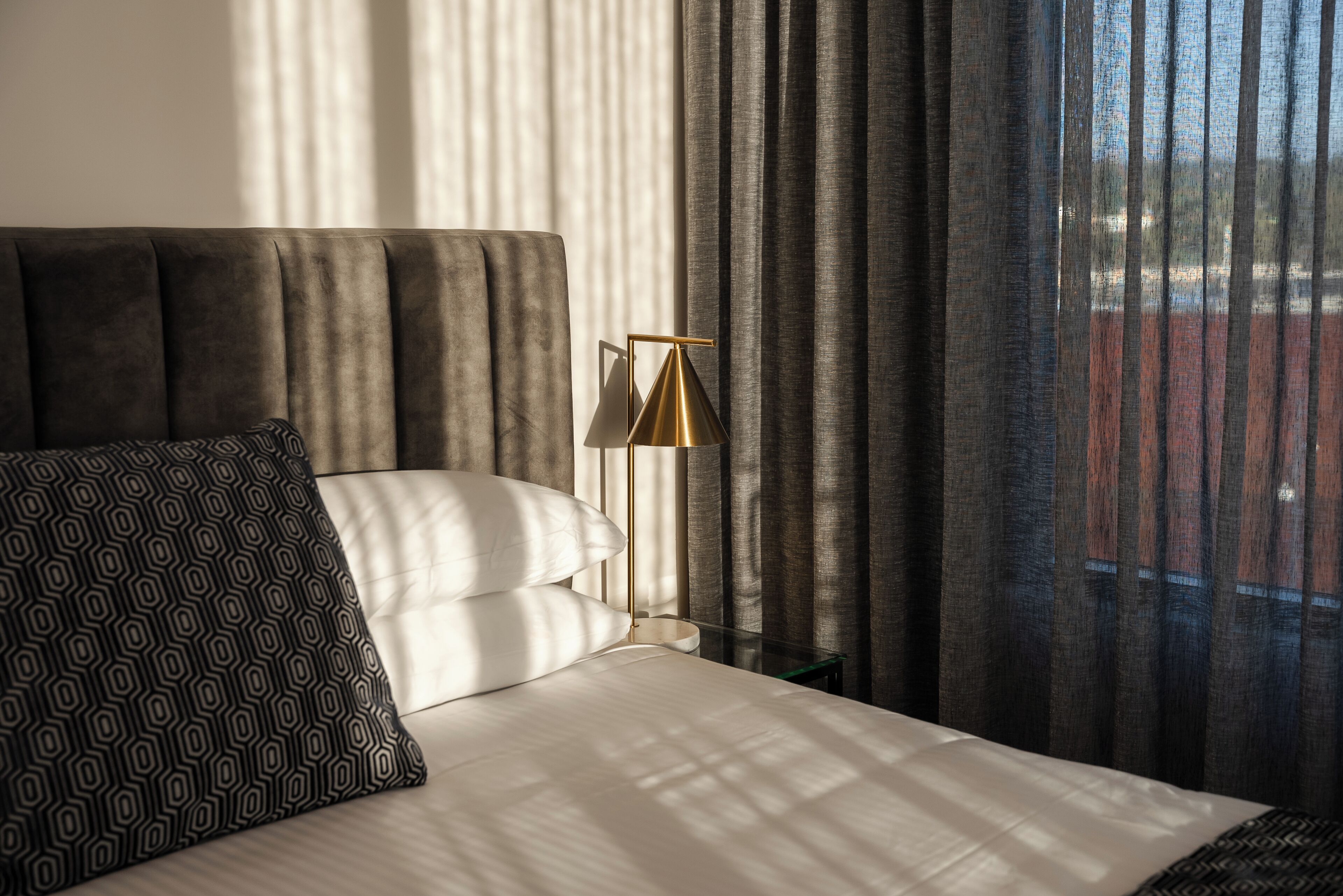 A neatly made bed with a patterned pillow and a gold lamp beside it.