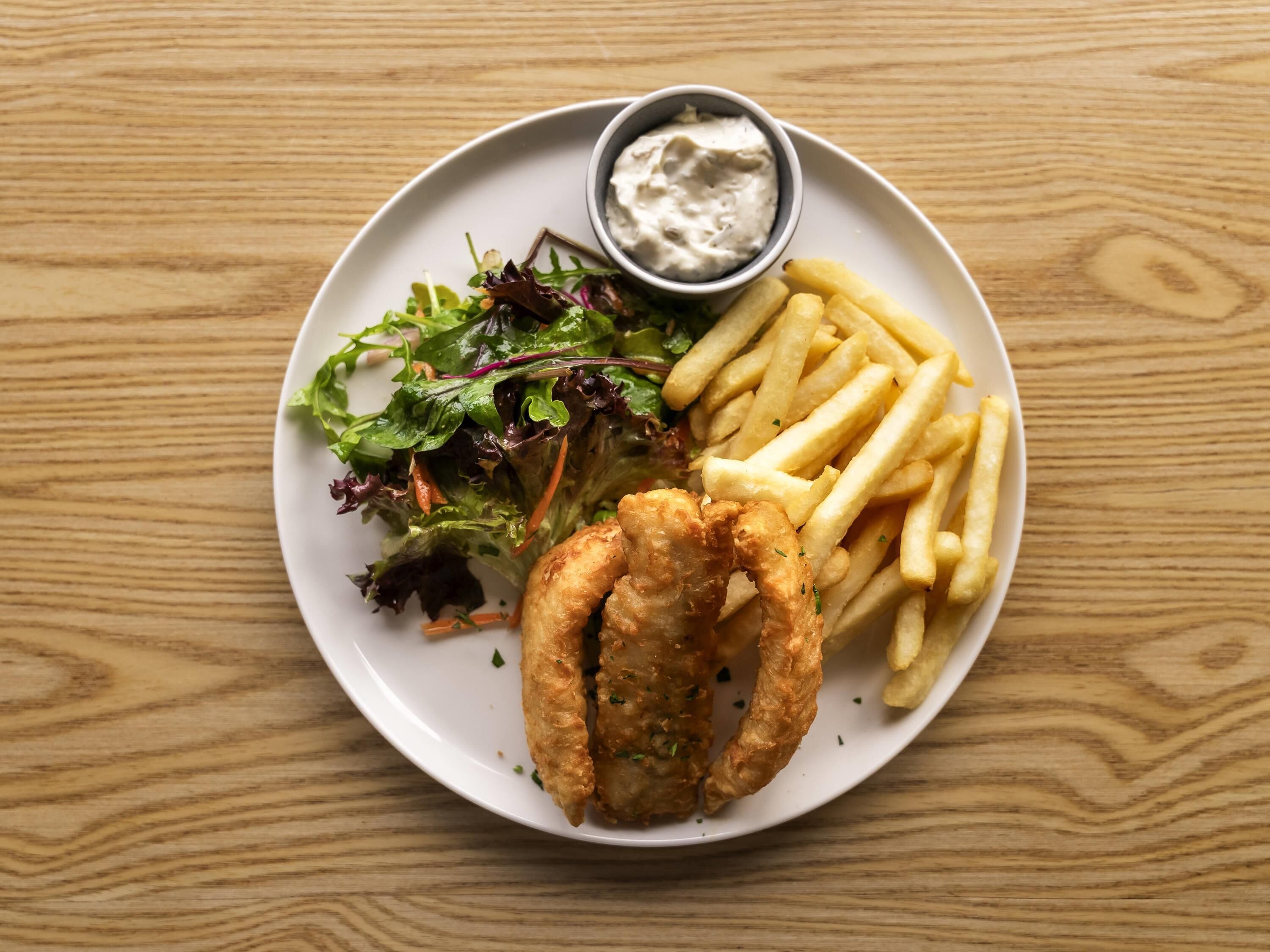 A plate with fish and chips, a salad, and a small bowl of sauce.