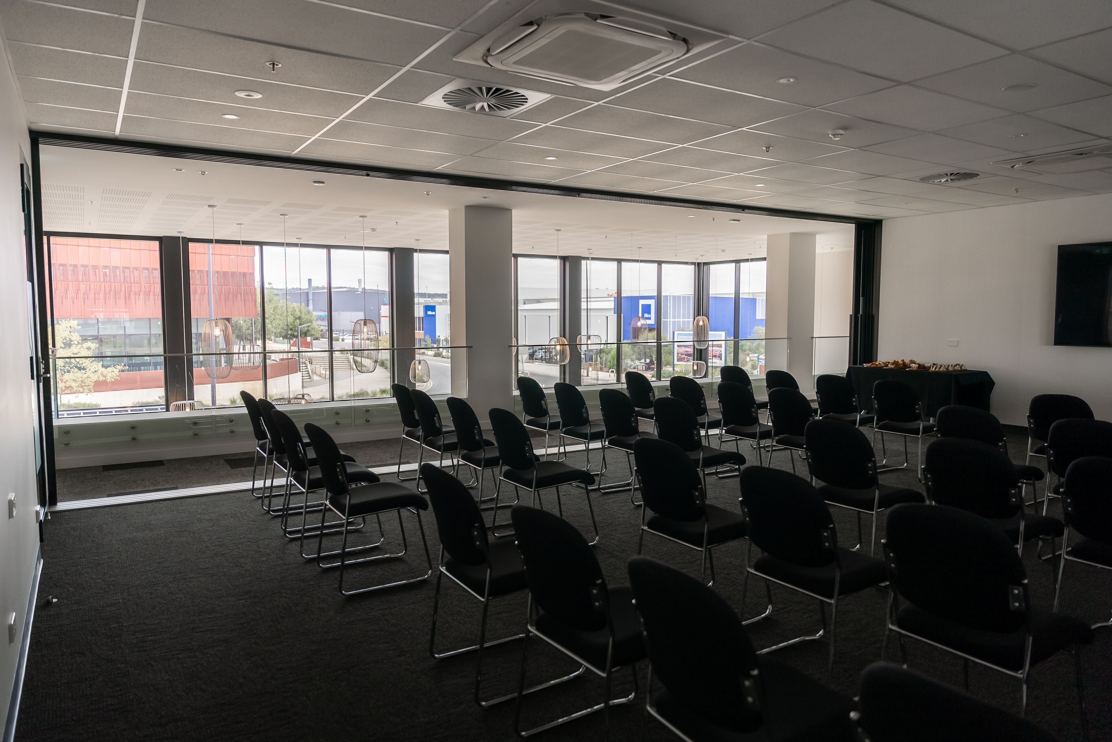 A conference room with rows of chairs, large windows, and a flat-screen TV on the wall.