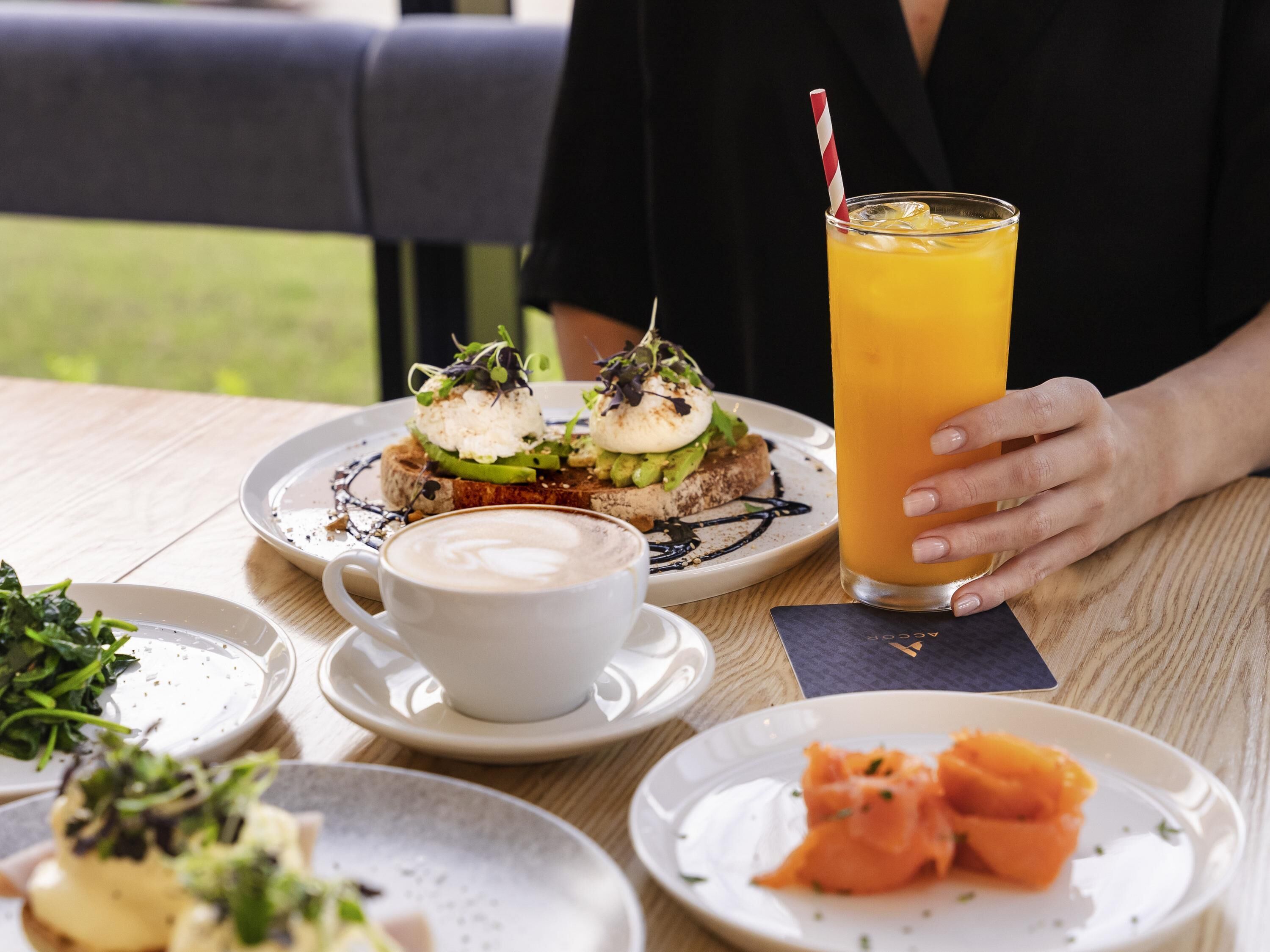 Une table à manger avec une assiette de nourriture, un verre de jus d’orange, une tasse de café et une serviette.