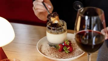 A dessert with a chocolate piece on a spoon, strawberries, and a glass of red wine on a table.