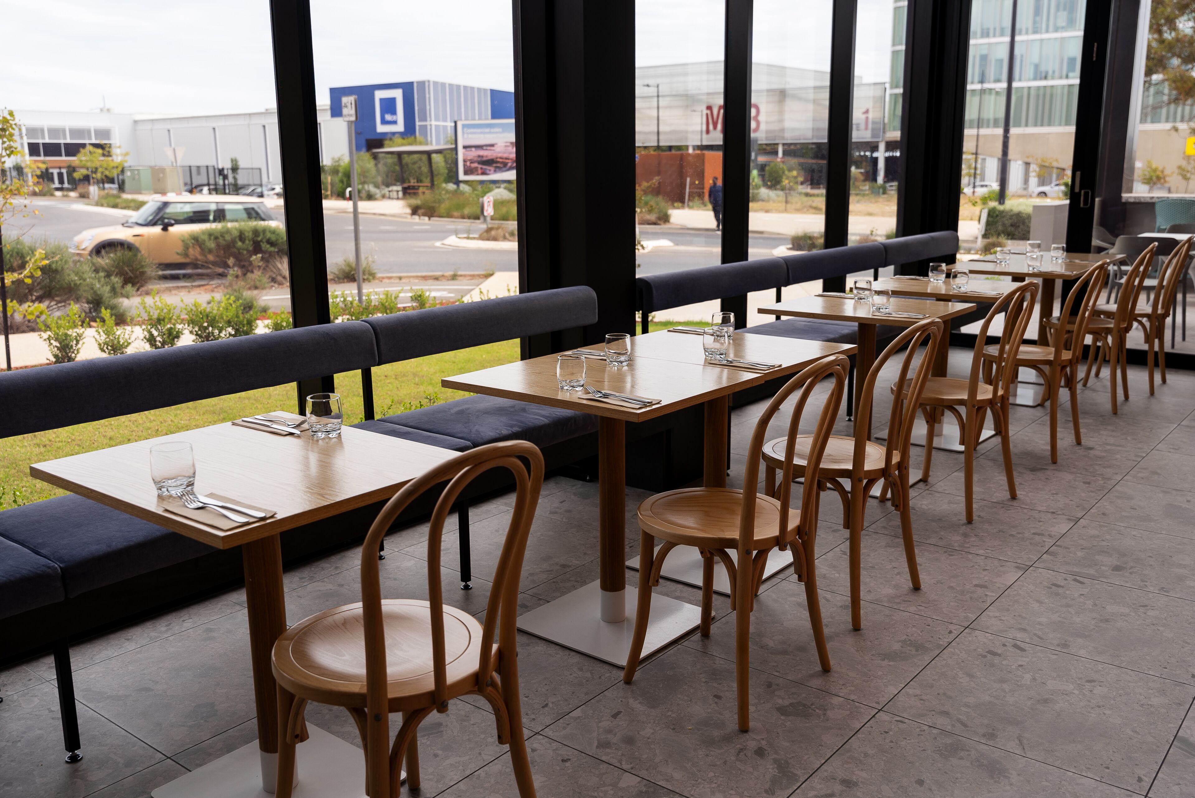 Un restaurante con terraza, mesas y sillas, y vista a la calle y edificios al fondo.