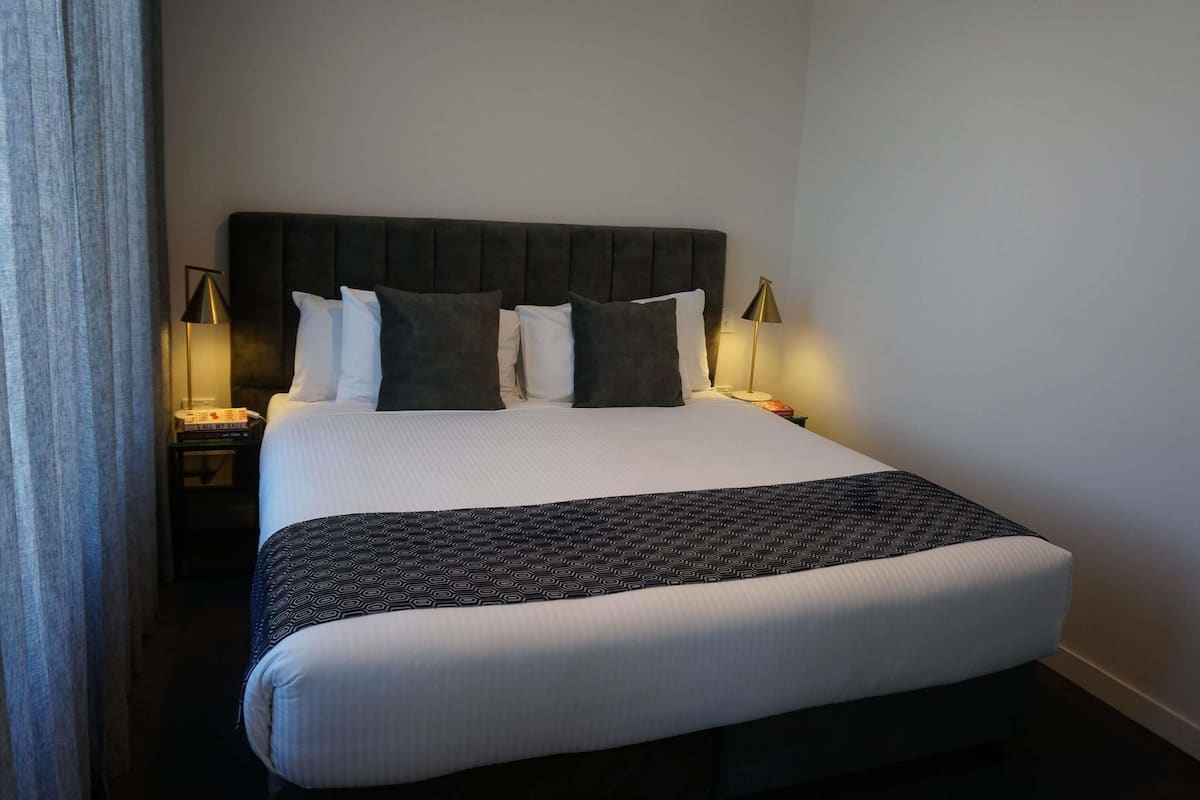 A neatly made bed with a patterned bedspread, a dark upholstered headboard, and two bedside lamps.