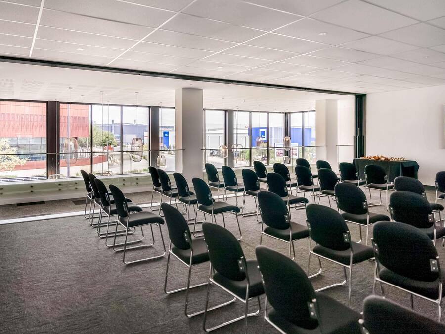 Un salón de conferencias con filas de sillas, ventanas amplias y una mesa con comida.