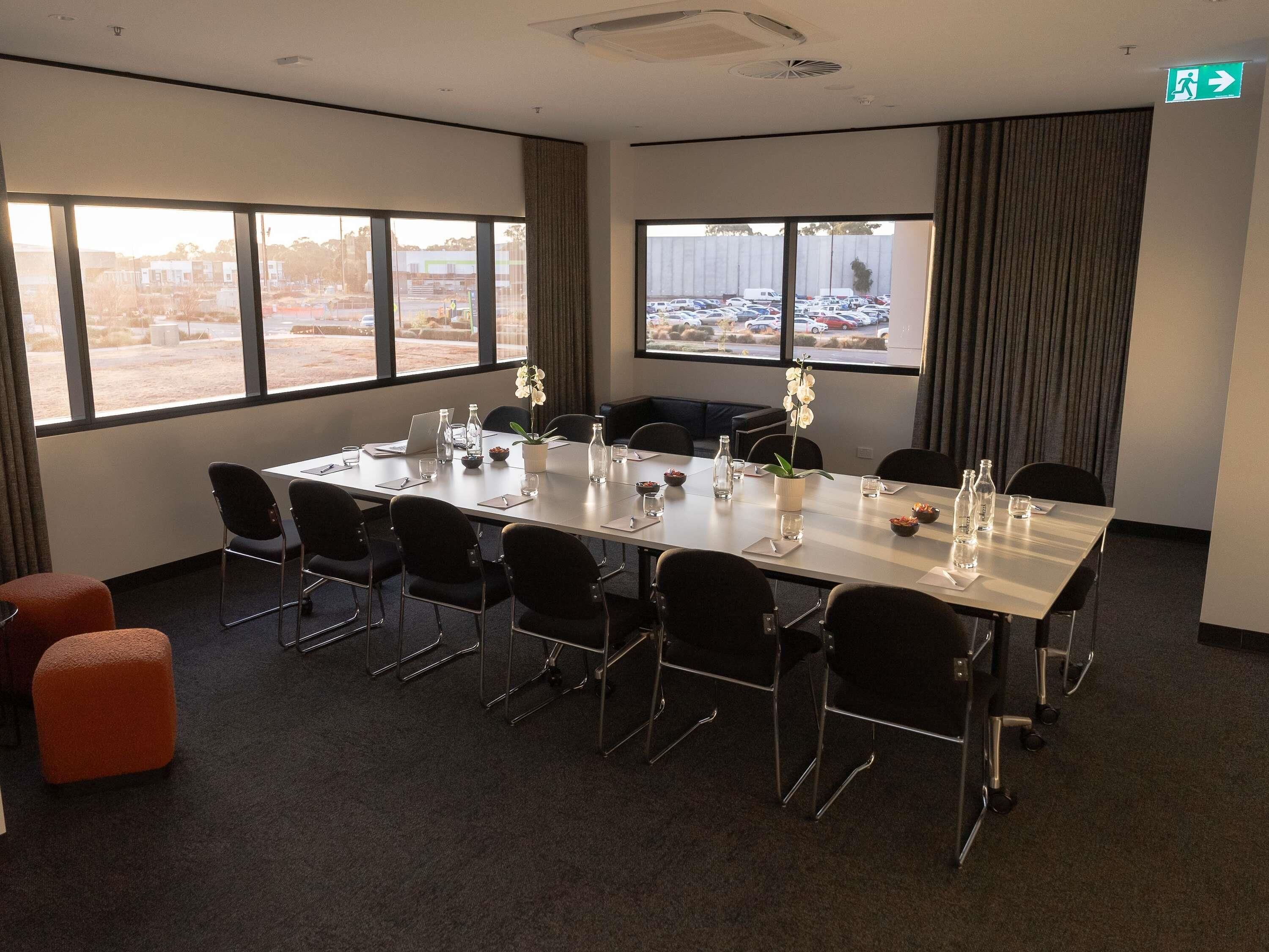 A conference room with a long table, chairs, a potted orchid, and a view of a parking lot through large windows.
