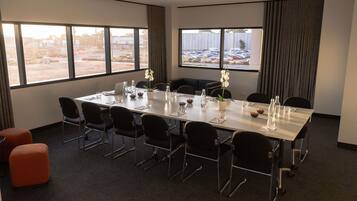 A conference room with a long table, chairs, a potted orchid, and a view of a parking lot through large windows.