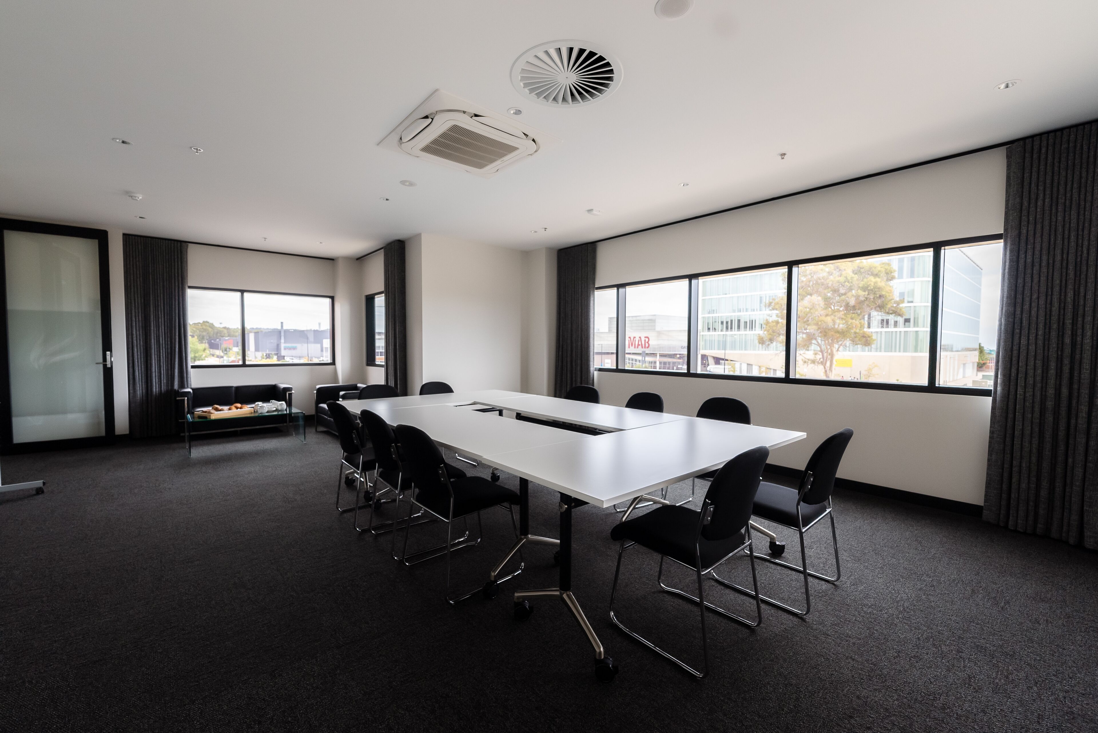 A conference room with a long table, black chairs, a sofa, and large windows with a city view.
