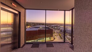 A modern elevator with a glass door, a view of a building complex, and a patterned wall. - Mantra Tonsley Adelaide (Tonsley)