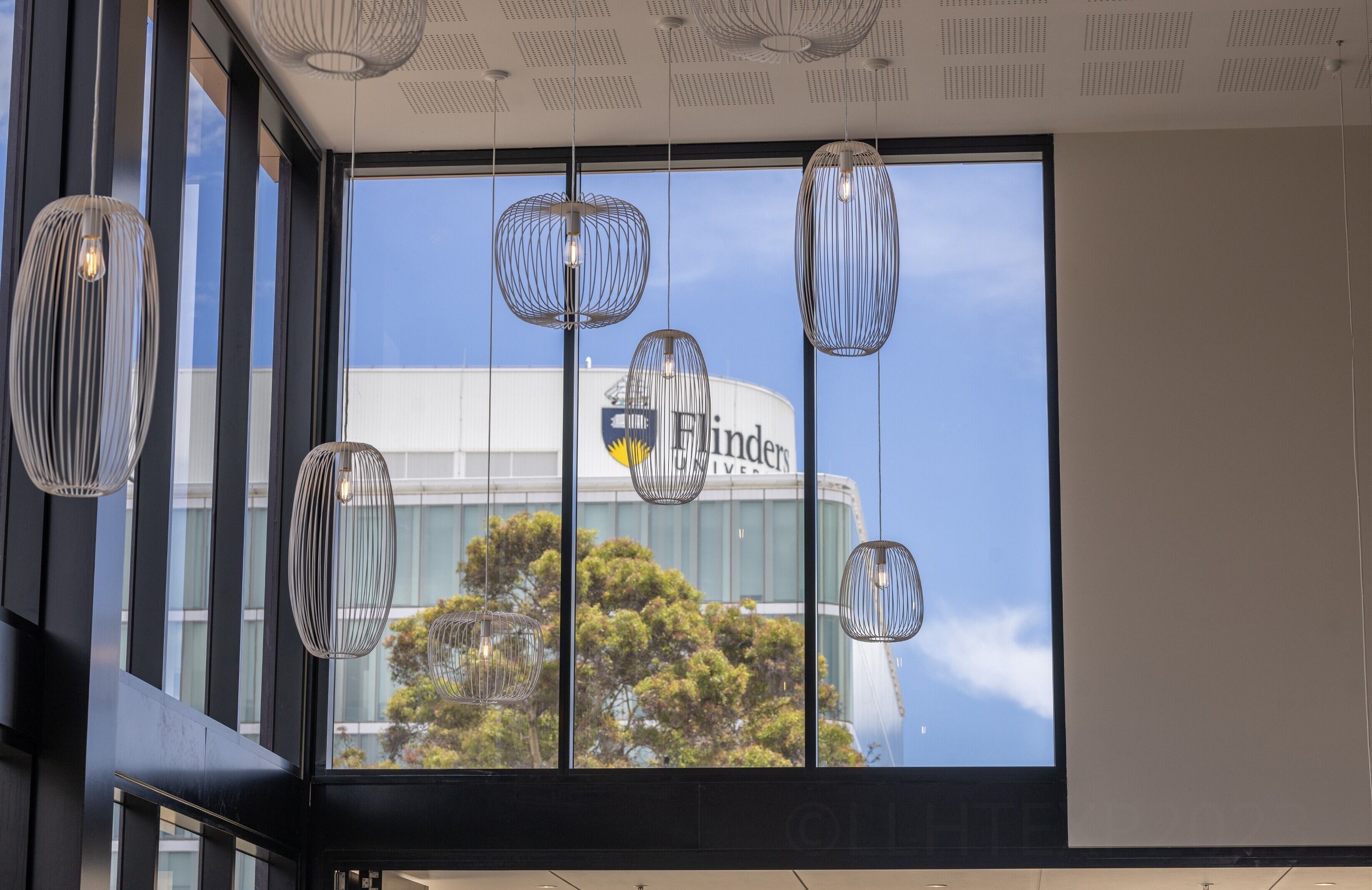 A modern interior with large windows, hanging pendant lights, and a view of a building with the name 'Flinders'.
