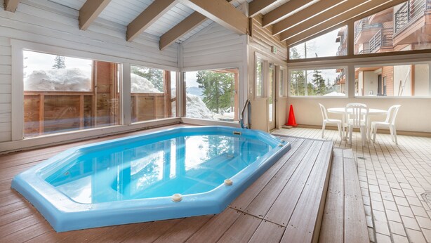 En inomhuspool med trägolv, stora fönster och ett bord med stolar.