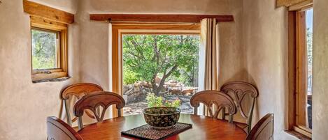 Un coin repas avec une table ronde en bois, quatre chaises, un luminaire en vitrail et une vue sur un arbre et des rochers, visible à travers une grande fenêtre.