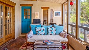 Ein gemütliches Zimmer mit einer blauen Tür, einem weißen Sofa mit gemusterten Kissen, einer hölzernen Bank und einem Vintage-Koffer auf einem Teppich.