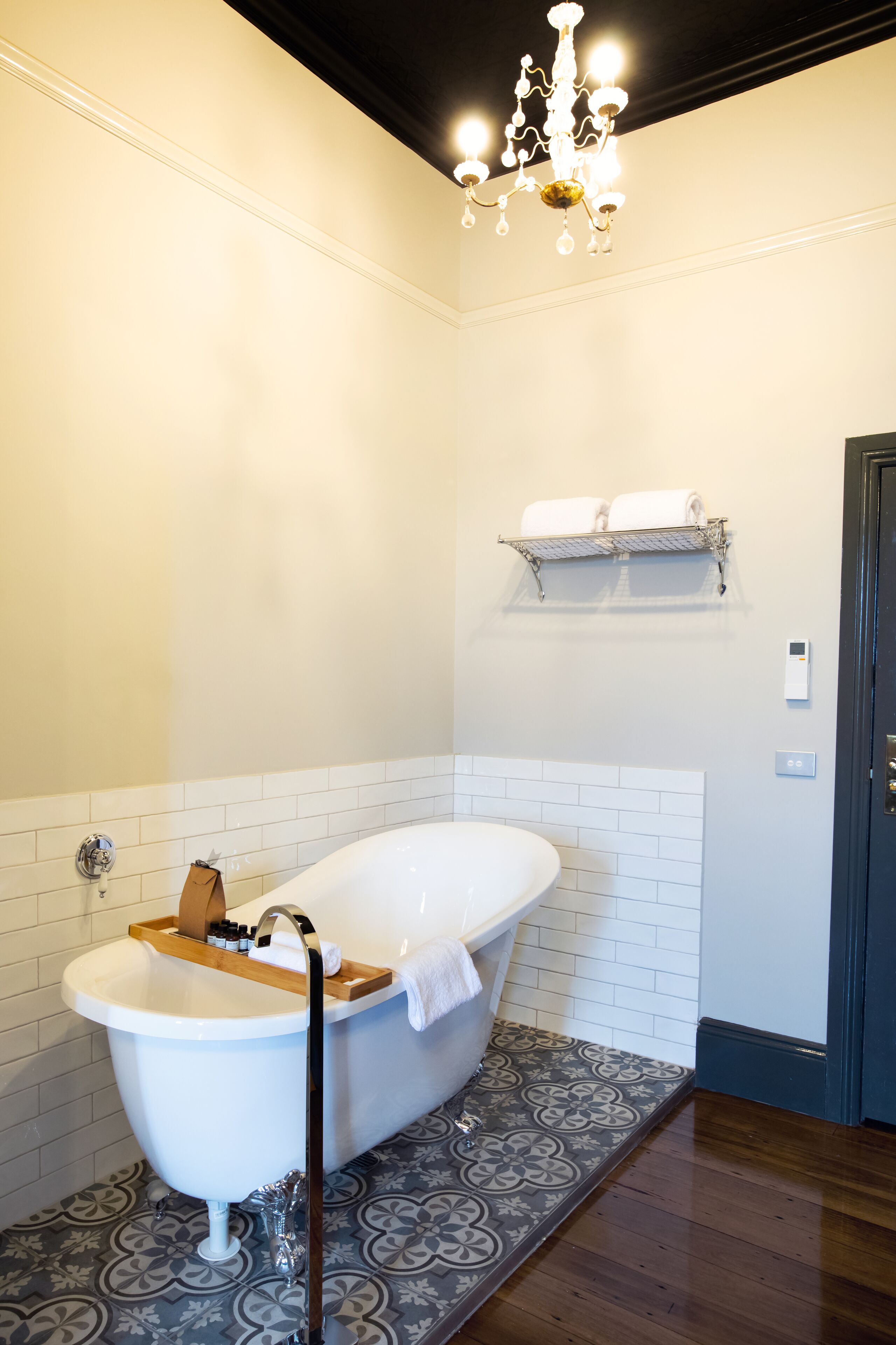 A bathroom with a freestanding bathtub, a wooden bath tray, a towel rack, and a patterned floor.