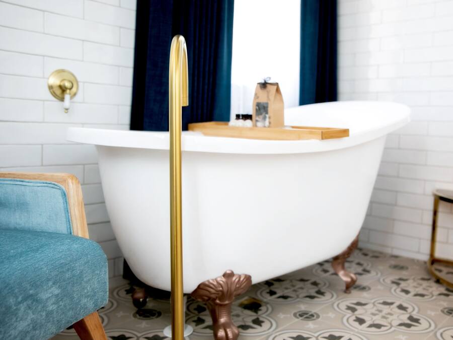 A bathroom with a white bathtub, a wooden chair, and a small table with toiletries.